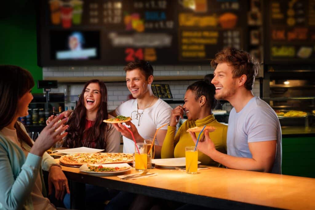 Cheerful multiracial friends having fun eating pizza in pizzeria for a fundraising event